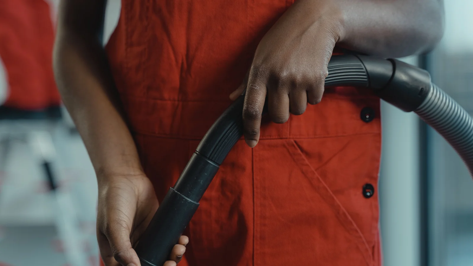 Close-up of hands holding a vacuum hose against red work clothing.
