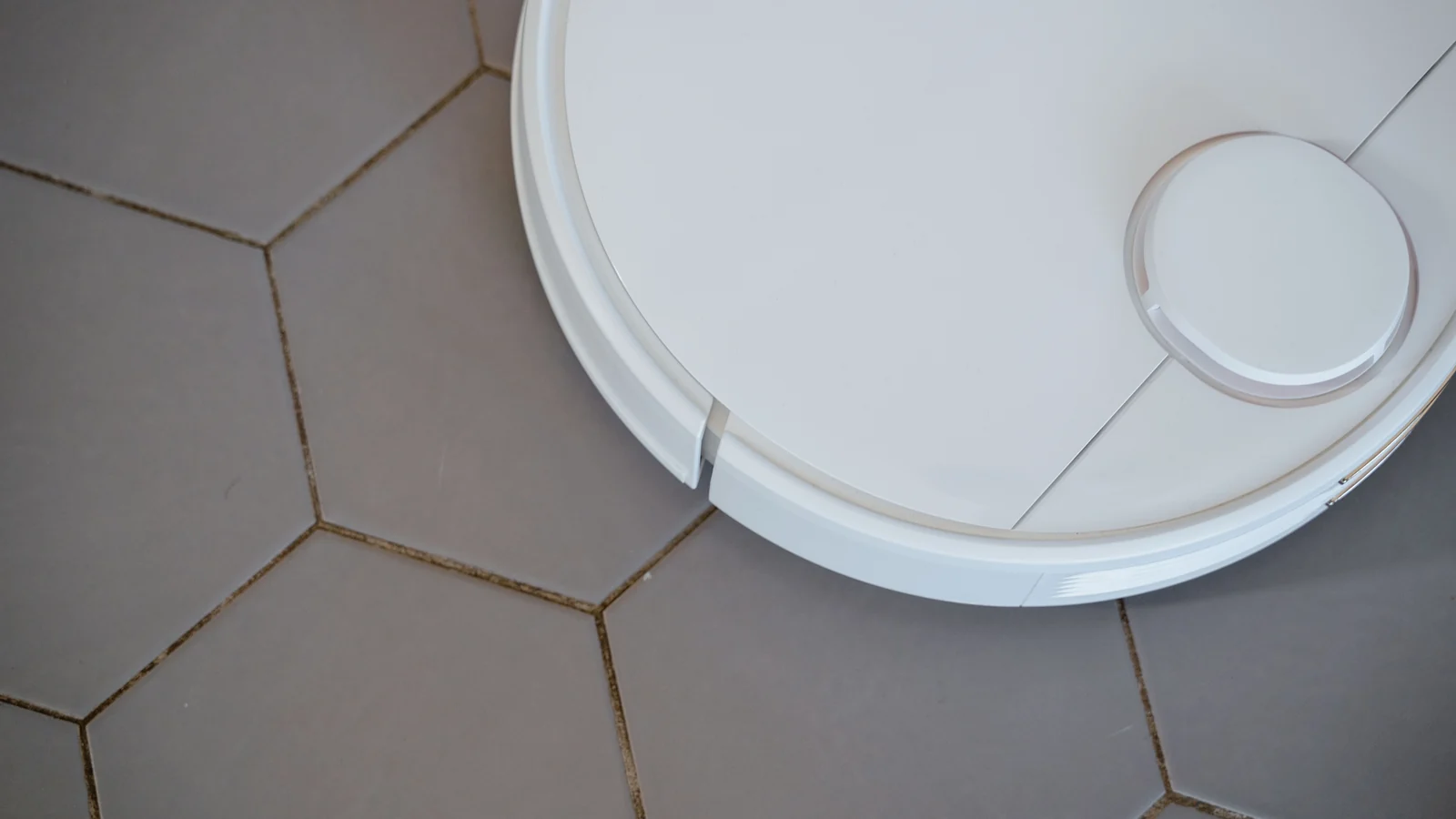 Overhead view of a white robot vacuum on hexagonal floor tiles.