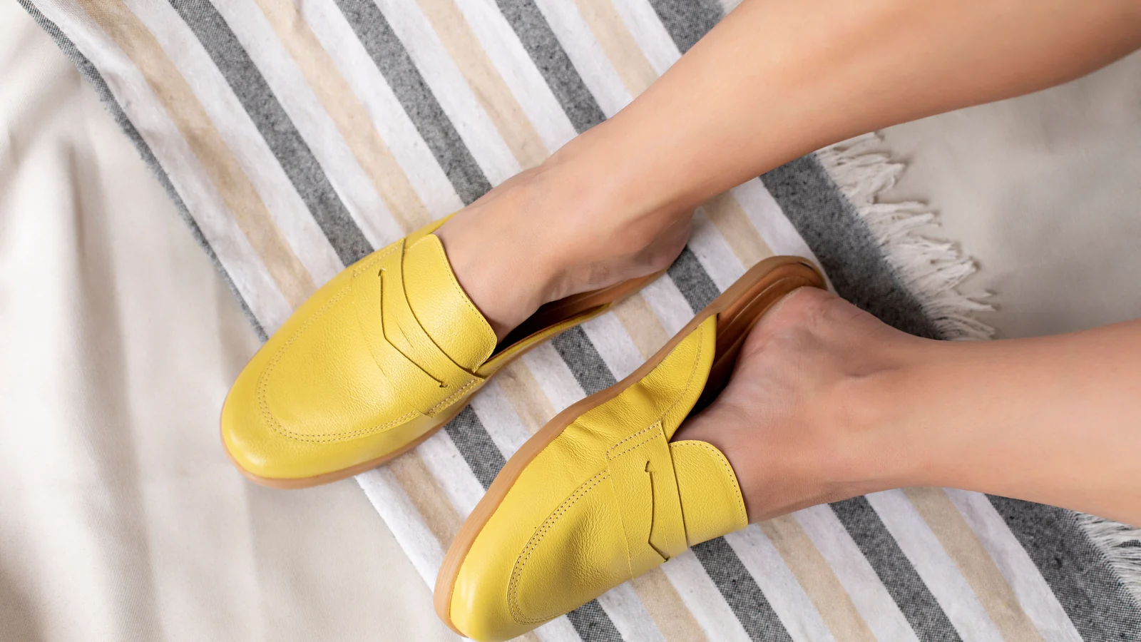 Illustrative stock image of feet wearing yellow loafers on striped fabric.