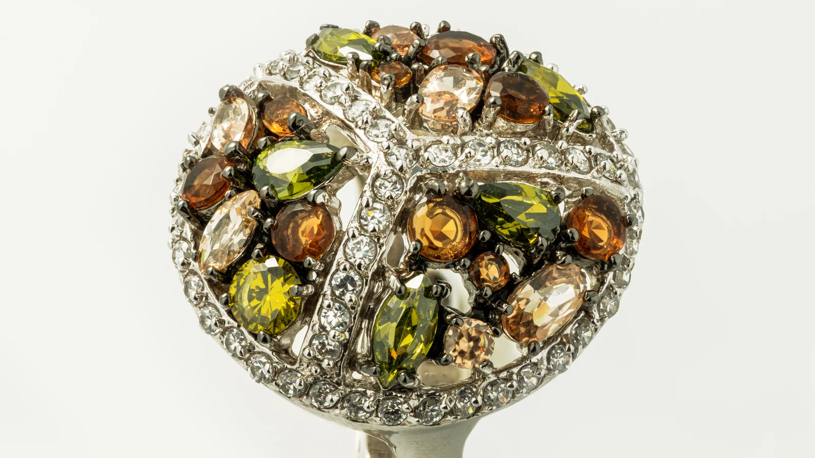 Close-up of a rounded ring set with green, amber-colored, and clear stones against a light background.